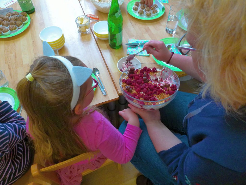 Mutter und Kind halten am GTisch eine Schüssel Süßspeise mit Früchten in der Hand